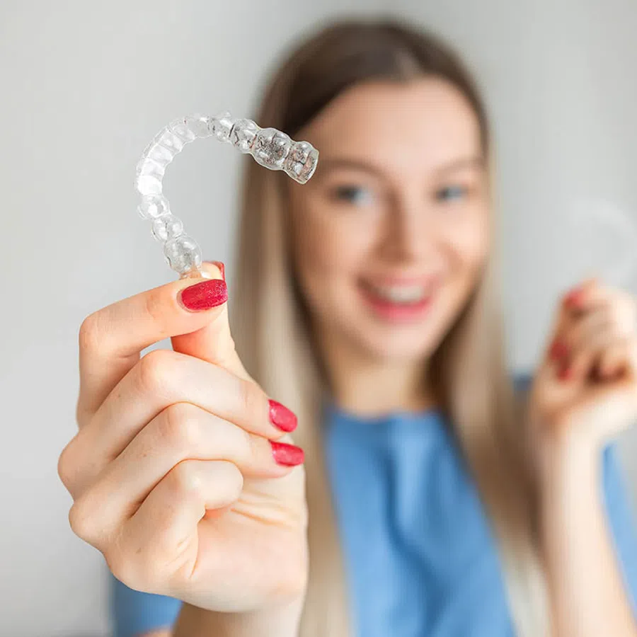 Smiling young woman with braces wearing a white off-shoulder sweater and a delicate necklace indoors.