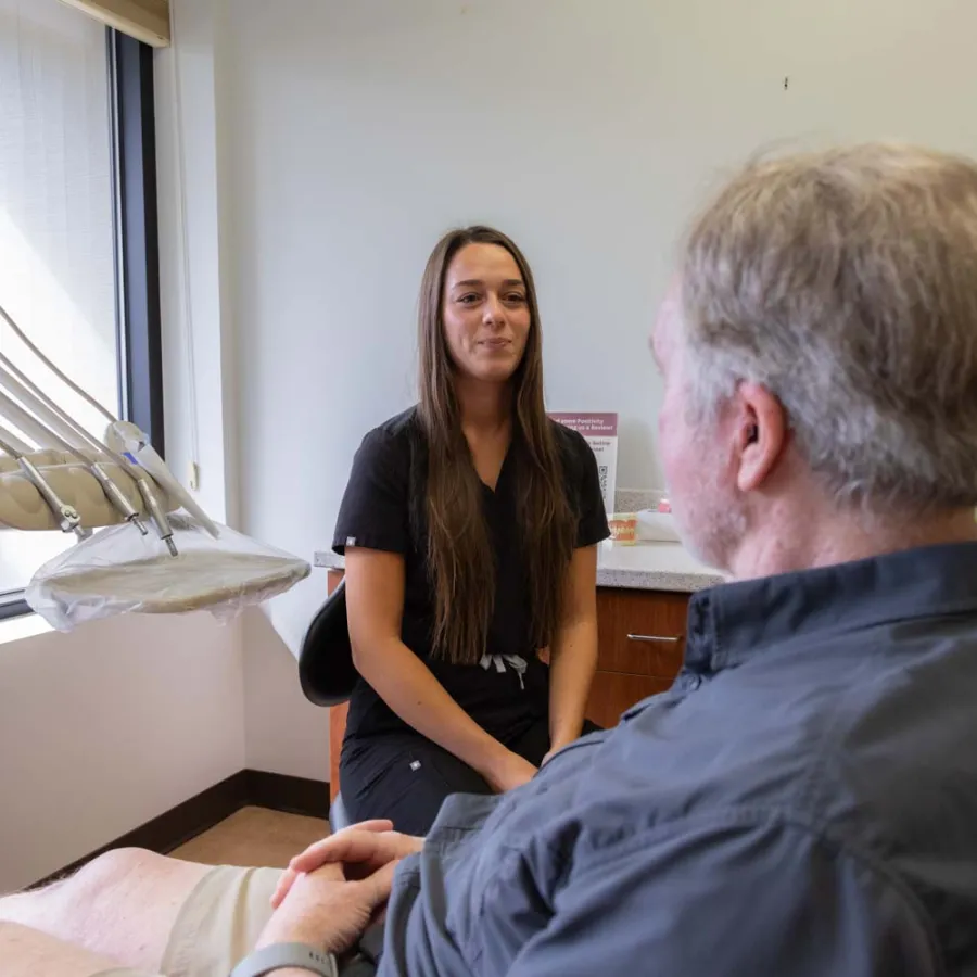Dentist or dental hygienist consulting with a male patient in a bright dental office near a window.
