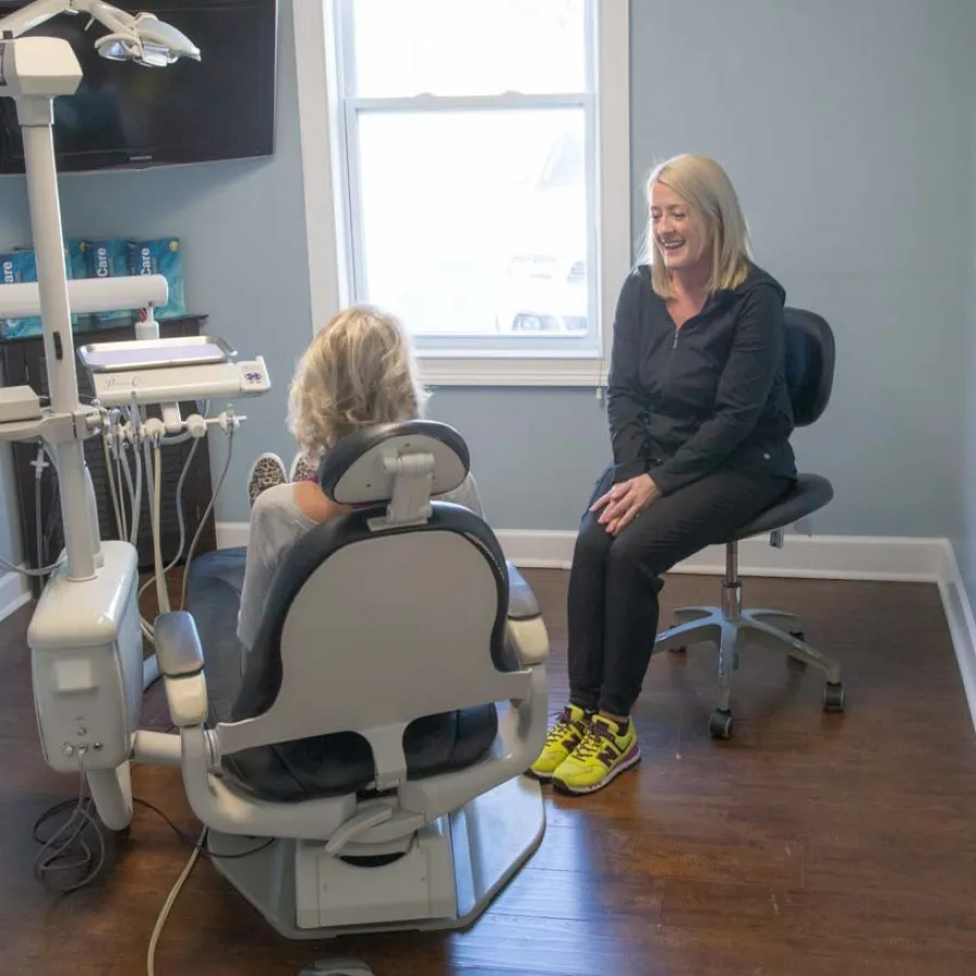Dentist consulting with a patient seated in a dental chair in a modern clinic room with wooden floor.