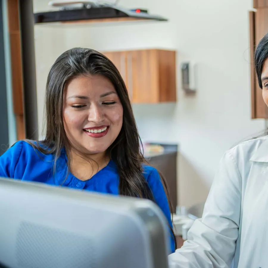 Female doctor and nurse reviewing medical information together on a computer in a clinic setting.