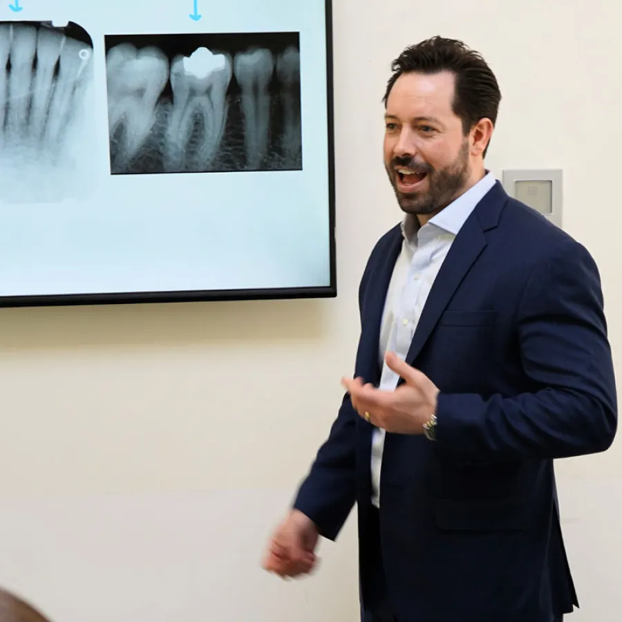 Dentist in suit explaining dental X-rays of teeth displayed on screen in a clinic setting.