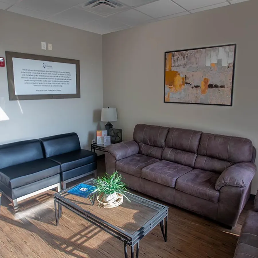 Modern waiting room with a brown leather couch, black leather chairs, coffee table, and abstract wall art.