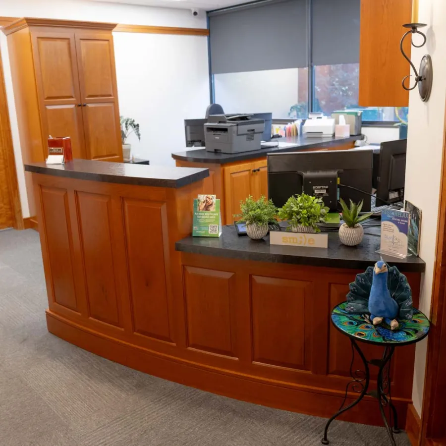 Reception area with wooden desk, office equipment, potted plants, and a decorative peacock statue on a small table.