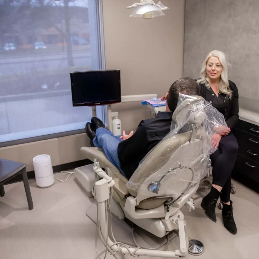 Dentist consulting male patient sitting in dental chair in modern clinic with window and TV screen
