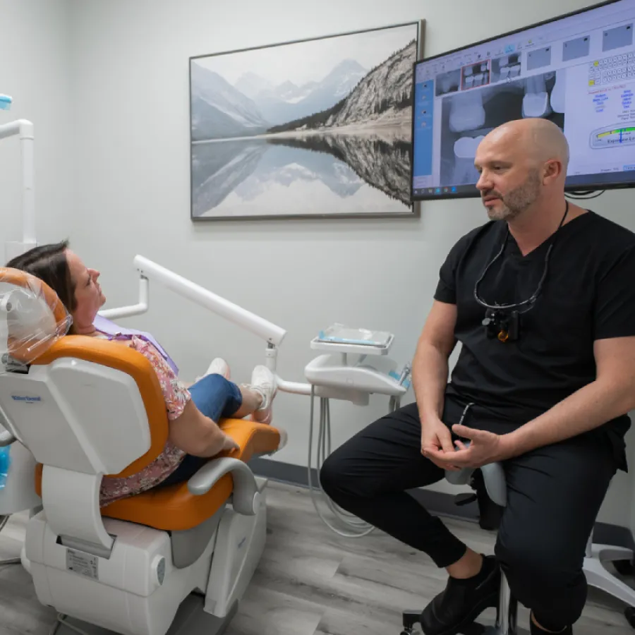 Dentist consulting female patient in dental office with X-ray images on screen and mountain art on wall