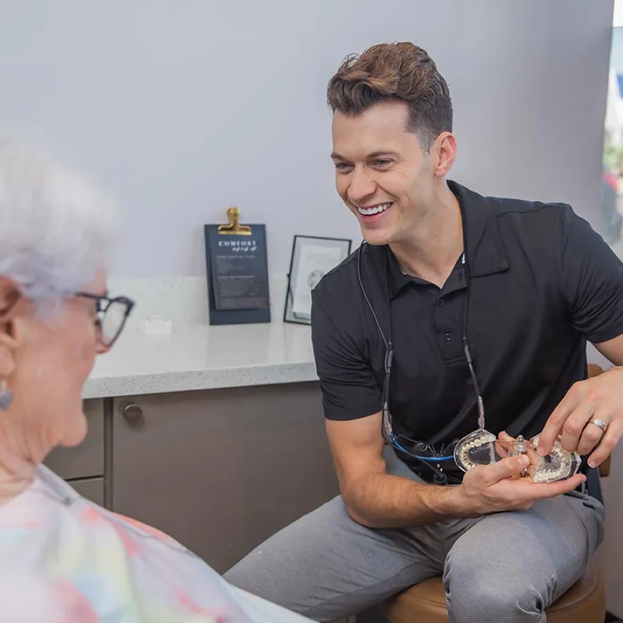 Female healthcare professional smiling while taking notes on clipboard during patient consultation in medical office.