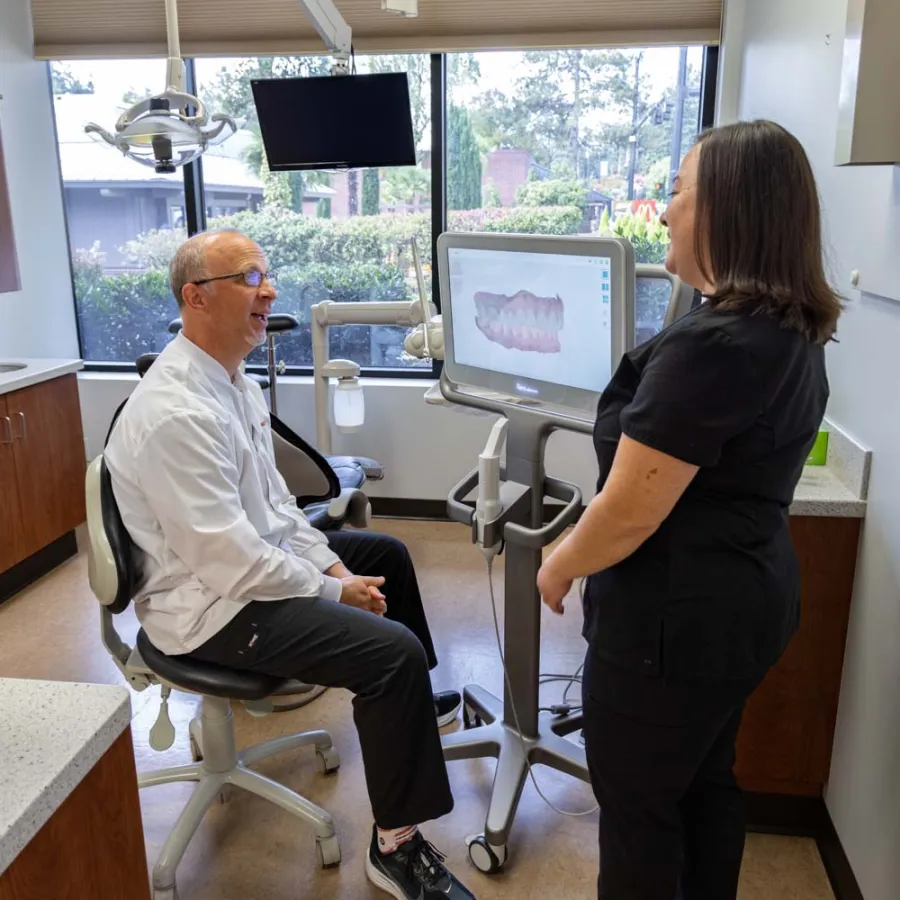 Dentist and assistant reviewing dental 3D scan images on a monitor in a modern clinic room with window views