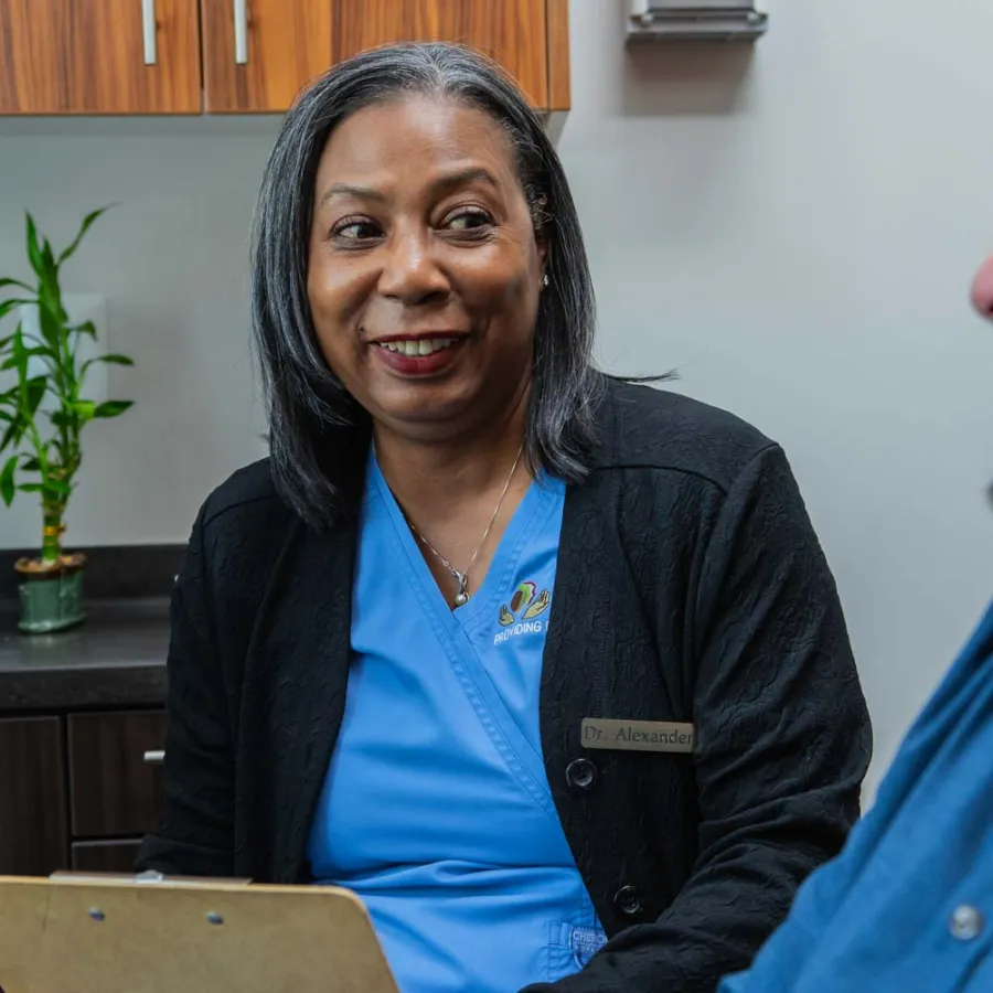Female doctor in blue scrubs smiling and talking with a male patient in a medical office.