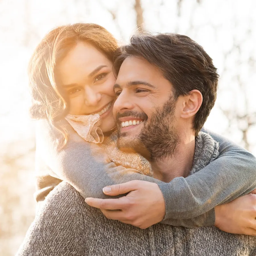 Happy couple embracing outdoors in cozy sweaters with warm sunlight in the background.