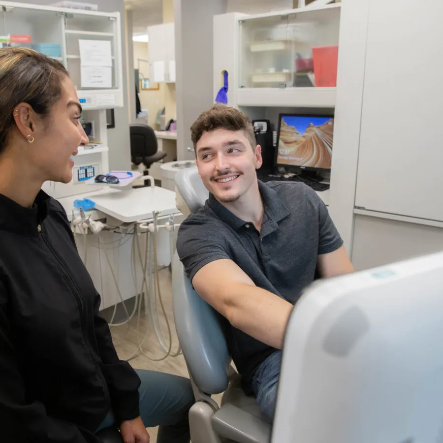 Male patient and female dental hygienist smiling and talking in a modern dental office setting.