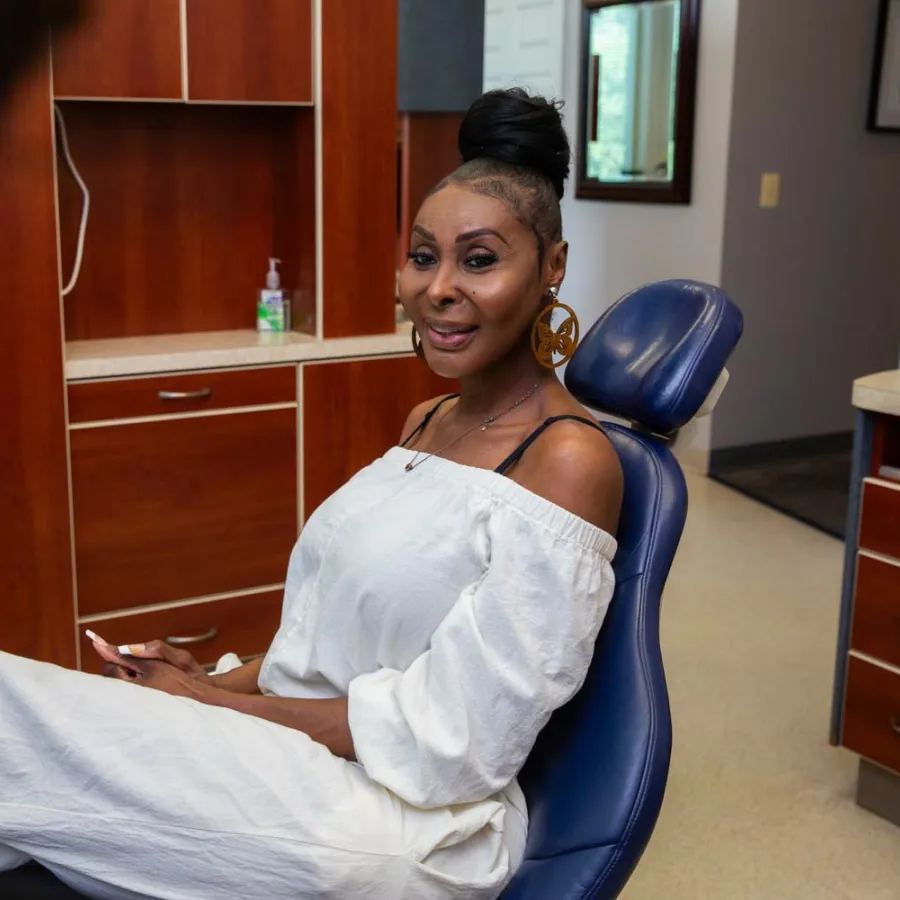 Woman in white outfit sitting in a dental chair smiling at the dentist in a clinic room