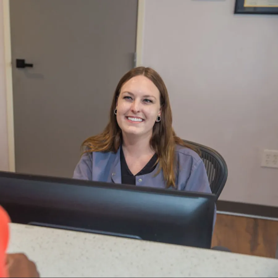 Smiling receptionist engaging with a visitor at a modern office front desk with computer and cabinets