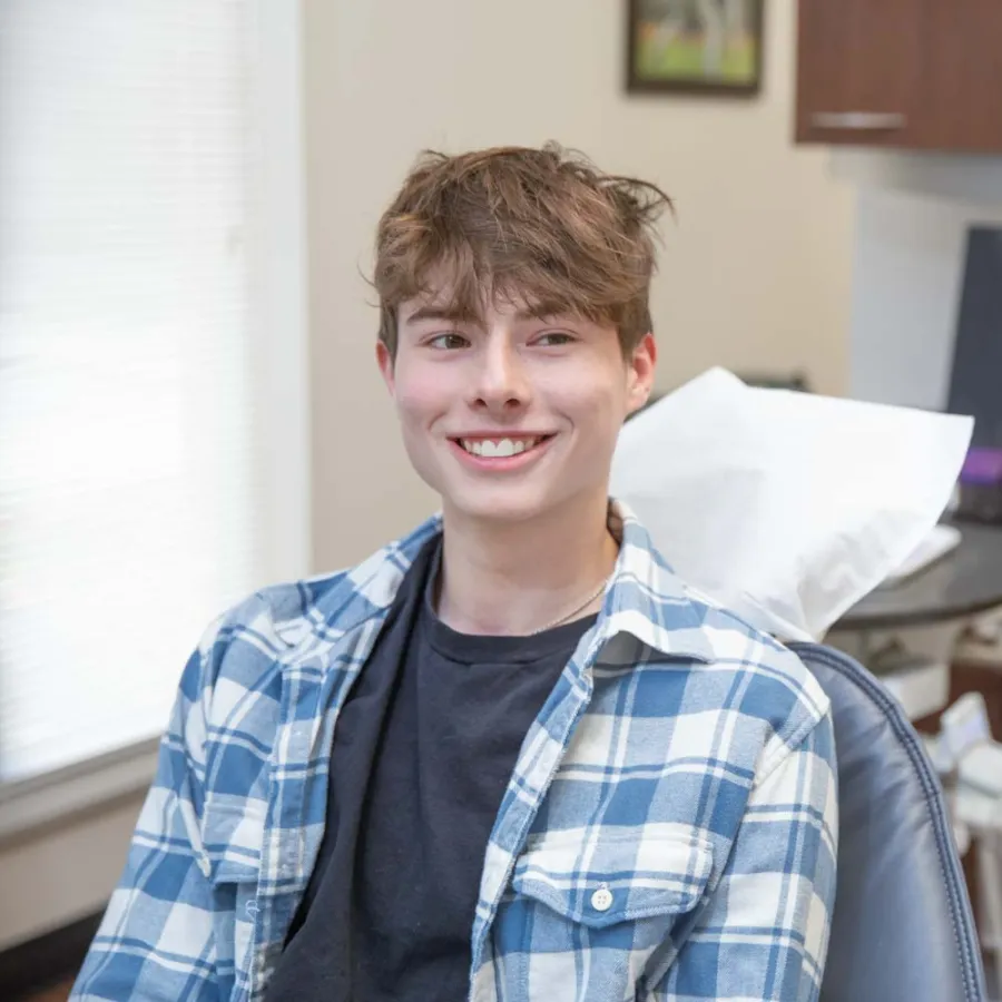 Teen boy smiling while sitting in dental chair during a checkup with dentist in clinic.