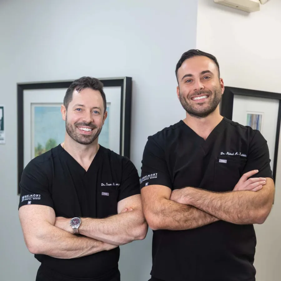 Two male doctors in black scrubs posing with arms crossed, smiling in a medical office setting.