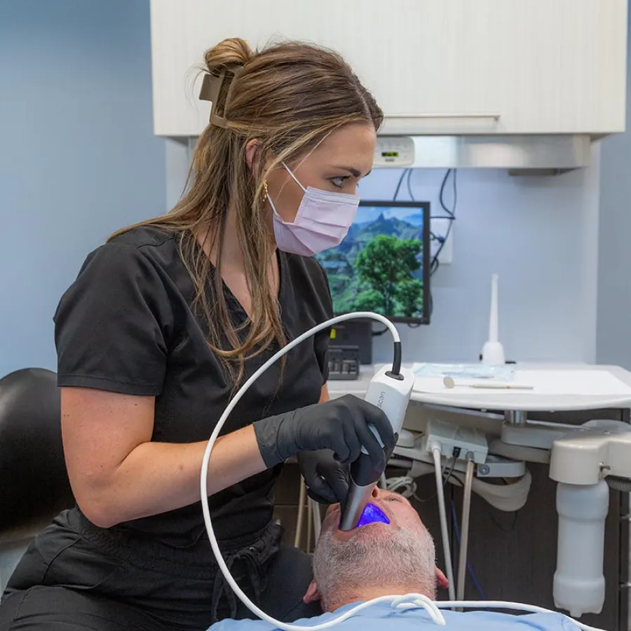 Dentist examining patient teeth with dental camera in modern clinic featuring clean blue walls and equipment.