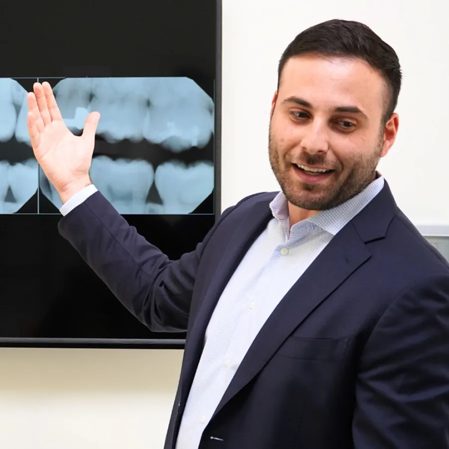 Dentist in suit explaining dental X-rays displayed on screen during consultation.
