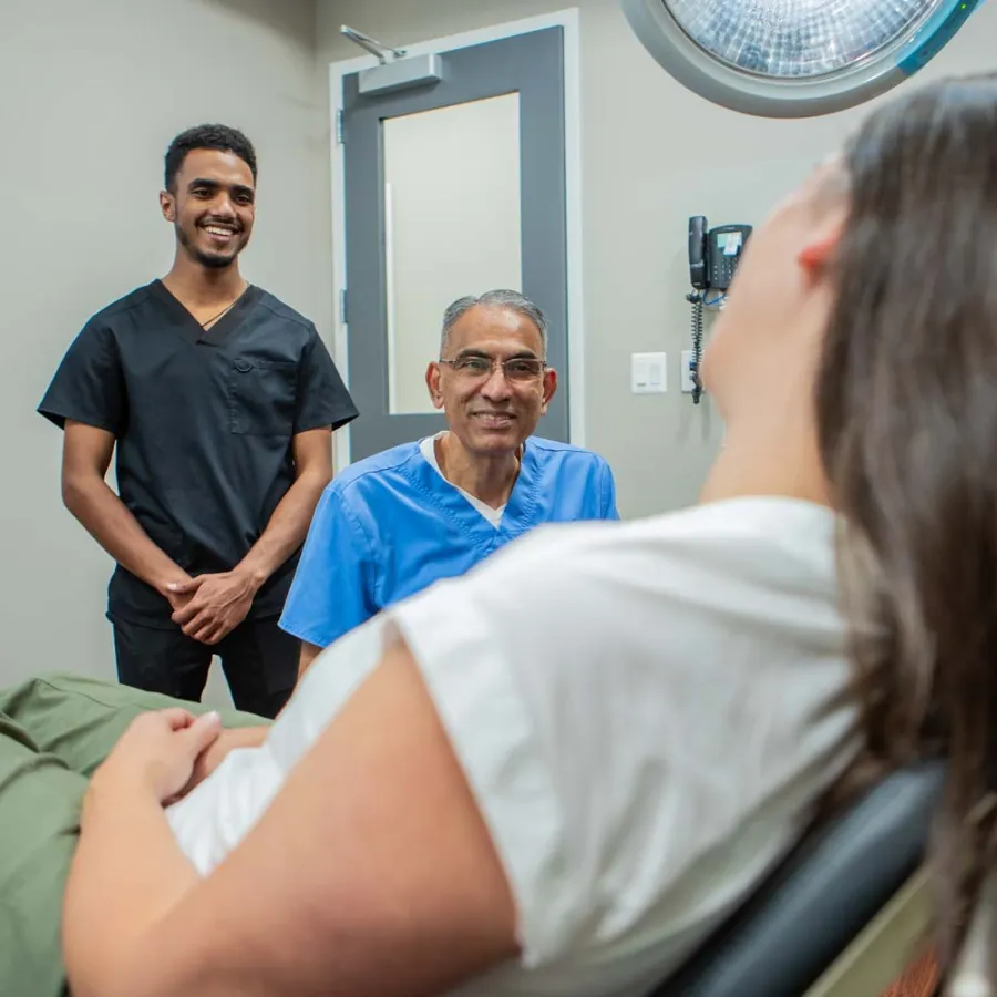 Patient reclining on exam chair with two healthcare professionals smiling in clinic room