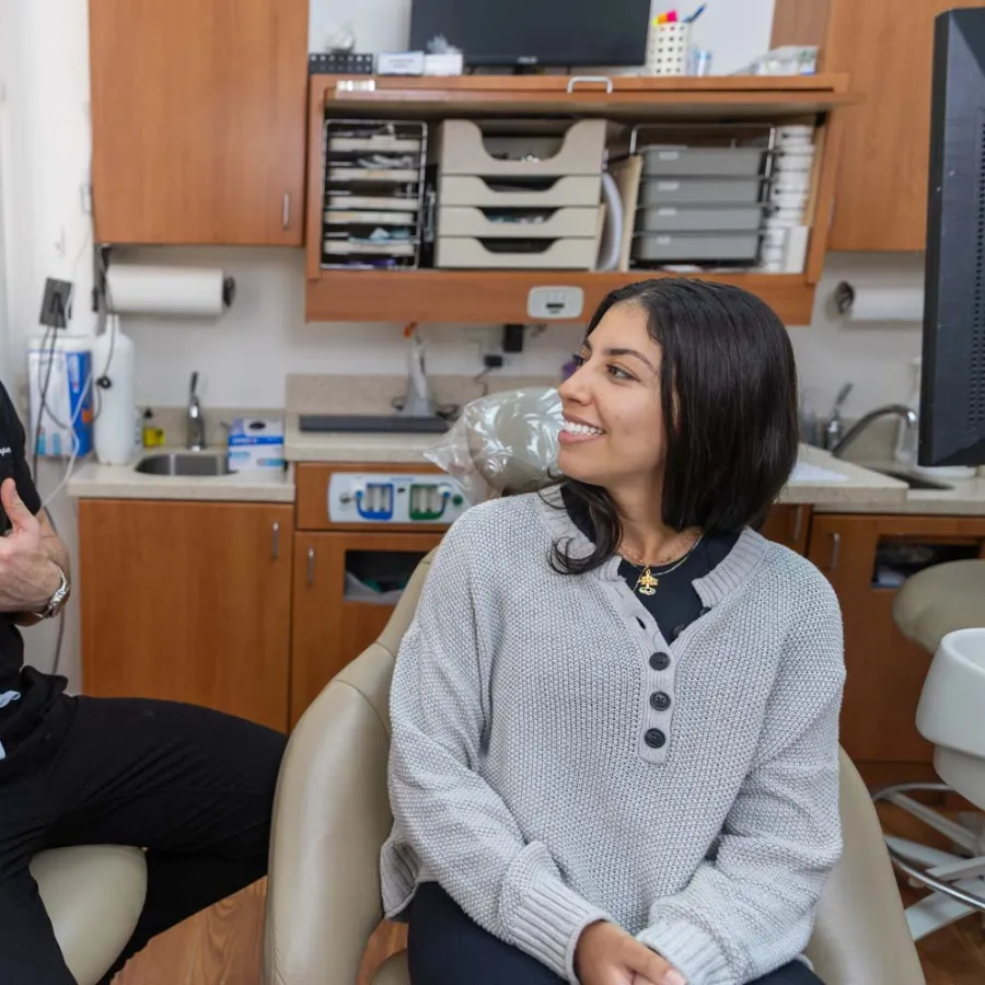 Dentist in black scrubs consulting and smiling with female patient seated in dental chair in modern clinic.
