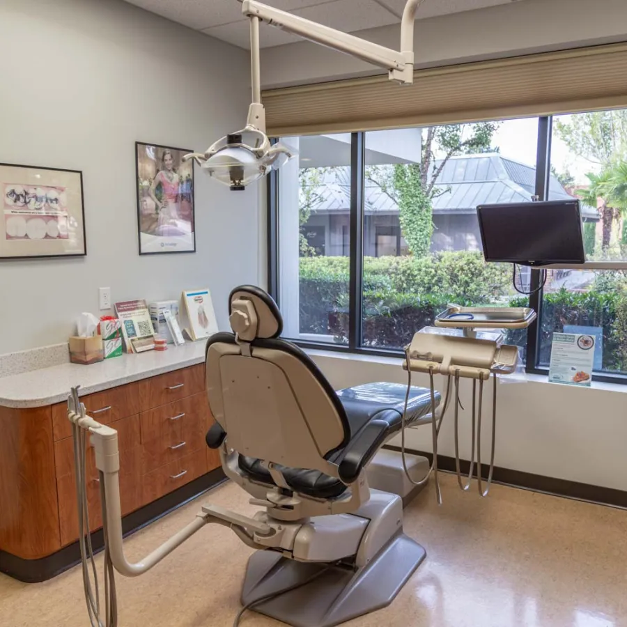 Modern dental office with a dental chair, equipment, large window, and outdoor view of greenery and buildings