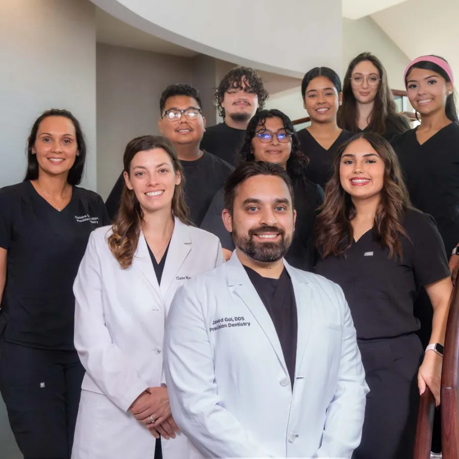 Group portrait of smiling dental team members in professional attire standing on a staircase inside a clinic