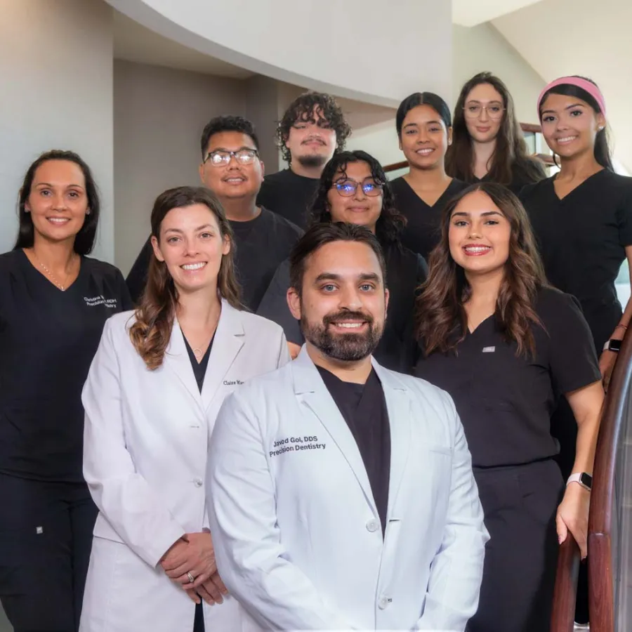 Group portrait of smiling dental team members in professional attire standing on a staircase inside a clinic