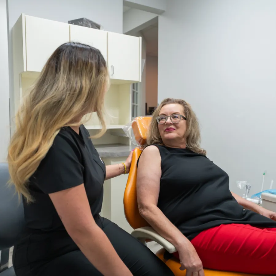 Dental professional consulting with a mature woman patient seated in an orange dental chair inside clinic.