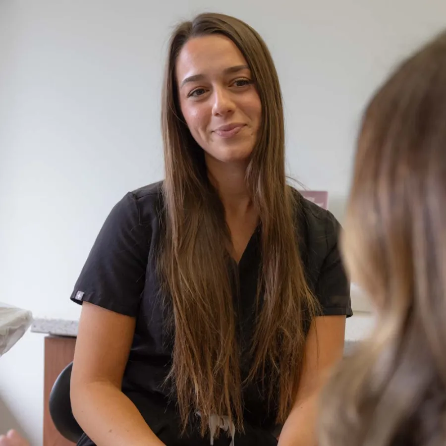 Smiling woman with long brown hair in black shirt conversing warmly with another person in indoor setting