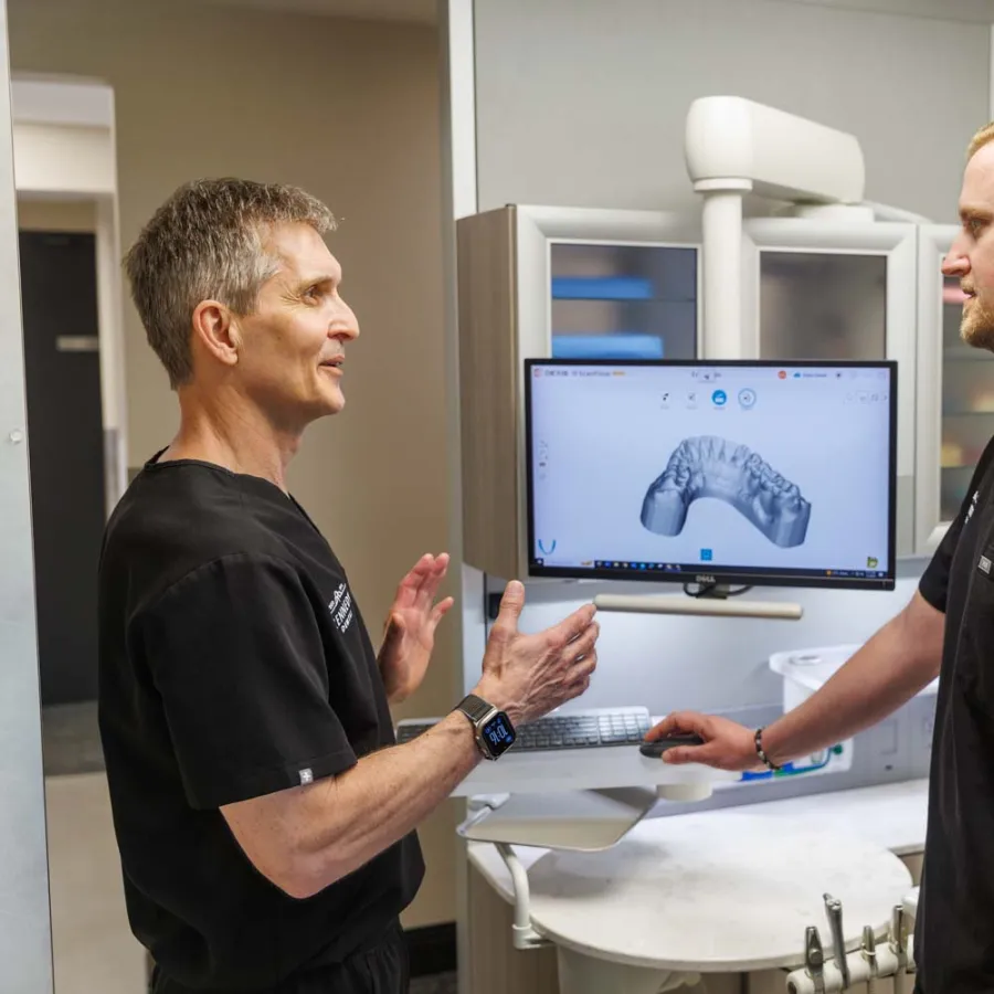 Two dental professionals discussing a 3D digital dental model displayed on a computer screen in a clinic.