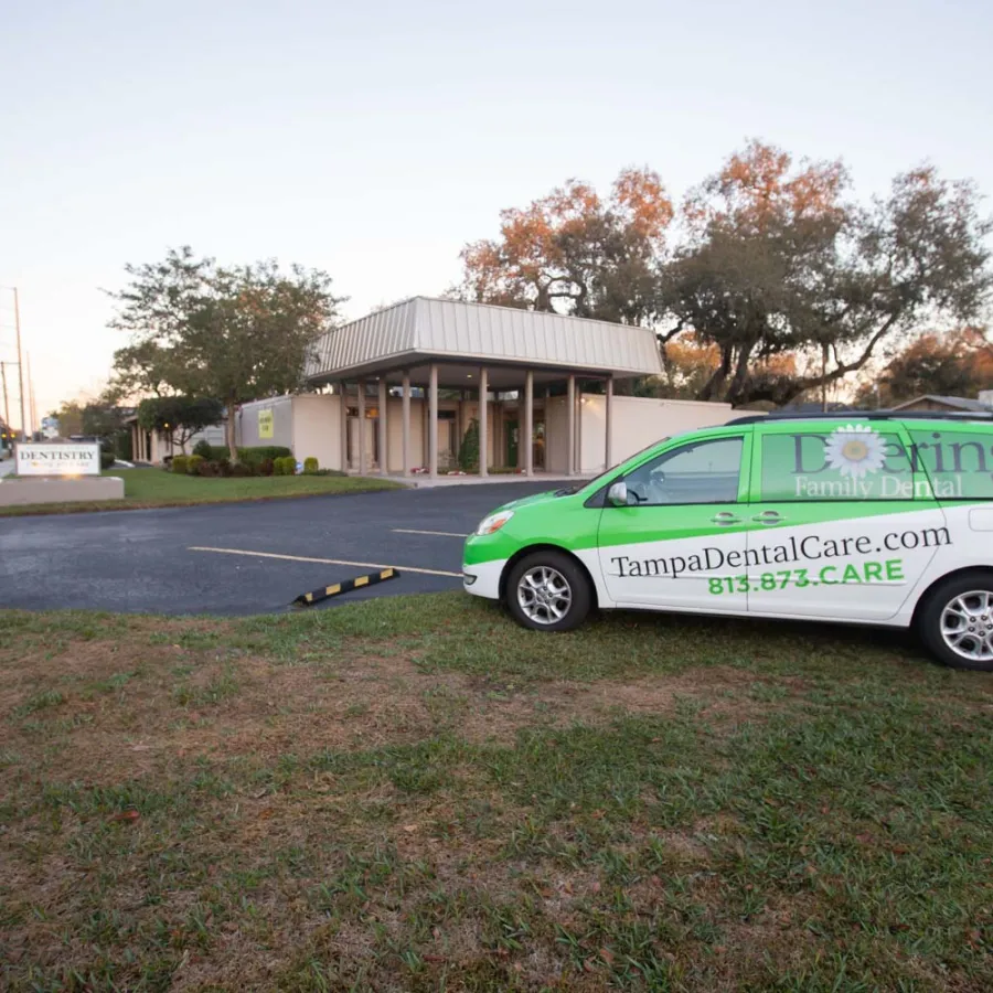 Green and white dental care company van parked in front of a modern dental office building at sunset.