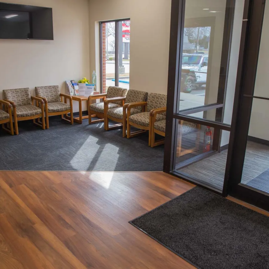 Waiting room with wooden chairs, a TV mounted on the wall, and glass doors letting in natural light
