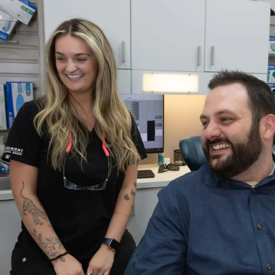 Smiling male patient and two female dental staff in a modern dental office with computer and medical supplies.