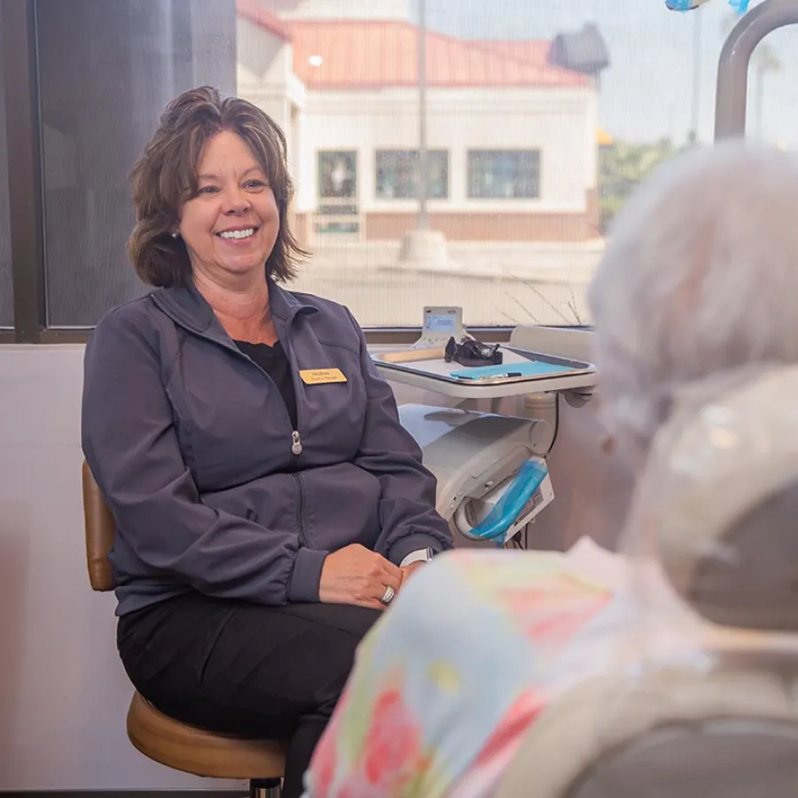Smiling healthcare professional in uniform consulting with elderly patient in a bright clinic room.