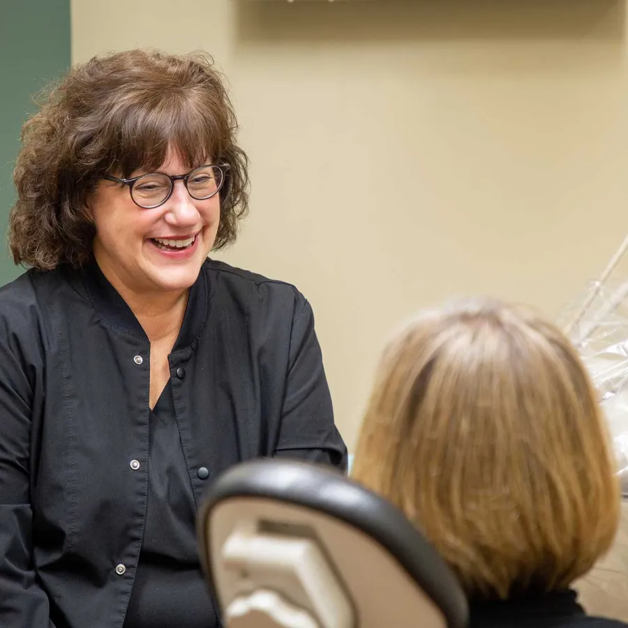 Smiling female dentist in black coat talking to female patient in dental office with equipment.