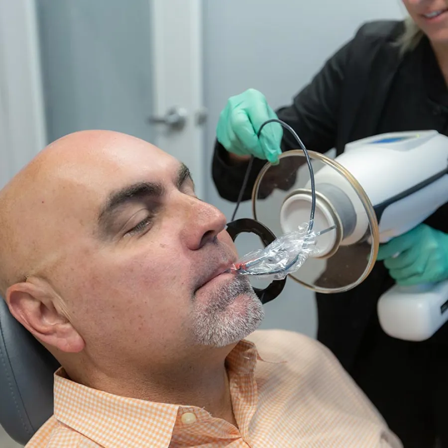 Man receiving a dental X-ray using a bitewing sensor and protective device in a dental office.