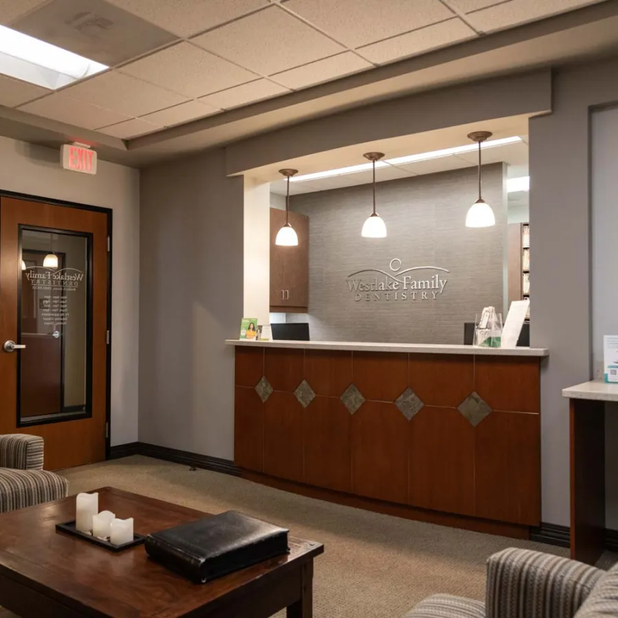 Reception area of Wesdale Family Dentistry with wooden desk, pendant lights, and comfortable seating.