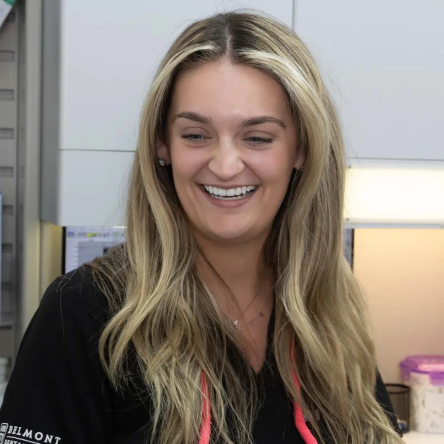 Smiling female healthcare worker with long blonde hair in black uniform at a medical office.