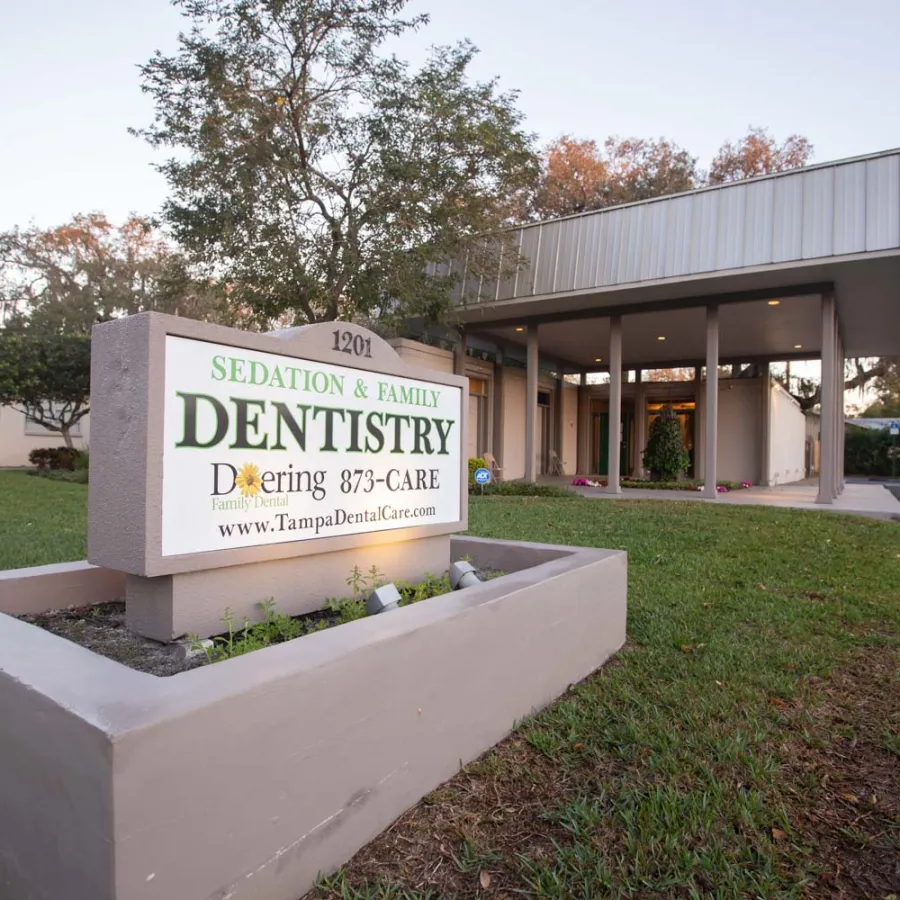 Sedation and Family Dentistry clinic sign outside a modern building with green lawn and trees under clear sky.