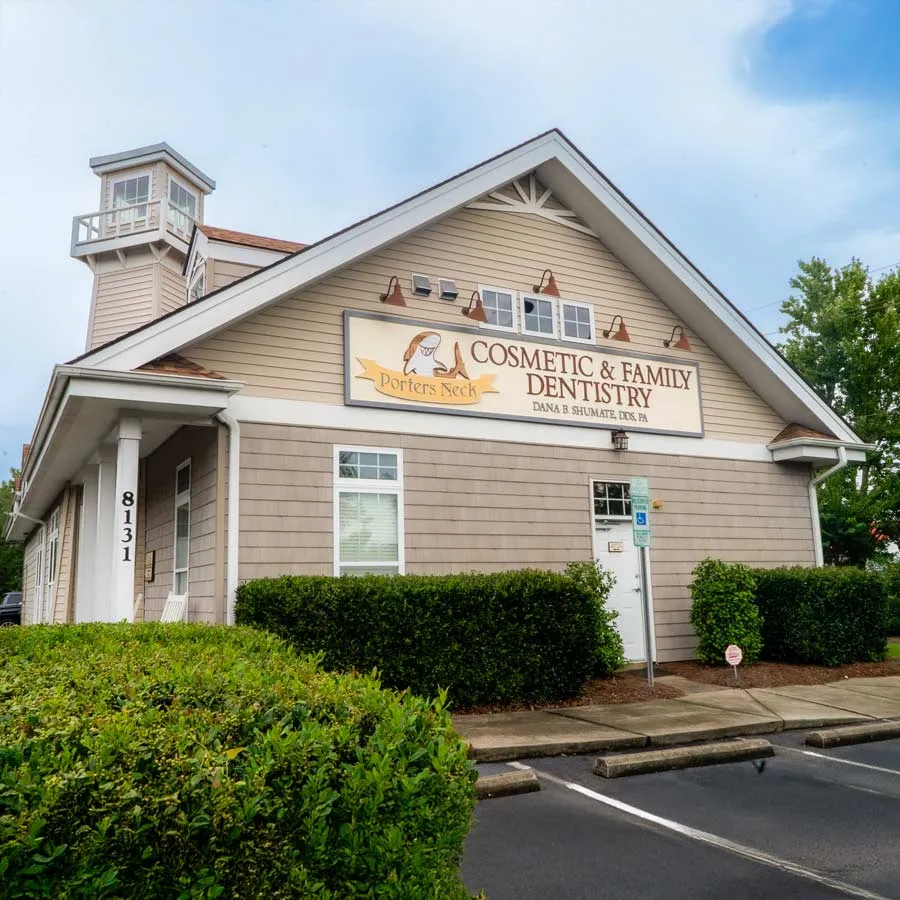Exterior view of Ports Neck Cosmetic & Family Dentistry building with parking and greenery on a clear day
