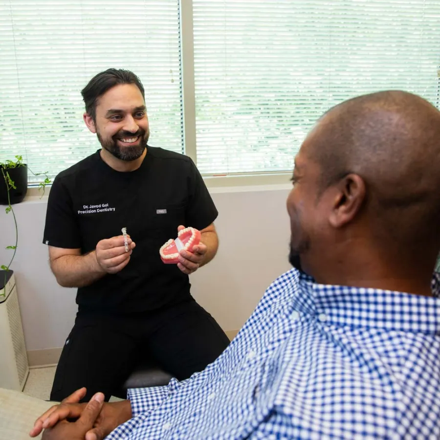 Dentist explaining dental procedure to a male patient using a teeth model in a dental clinic.