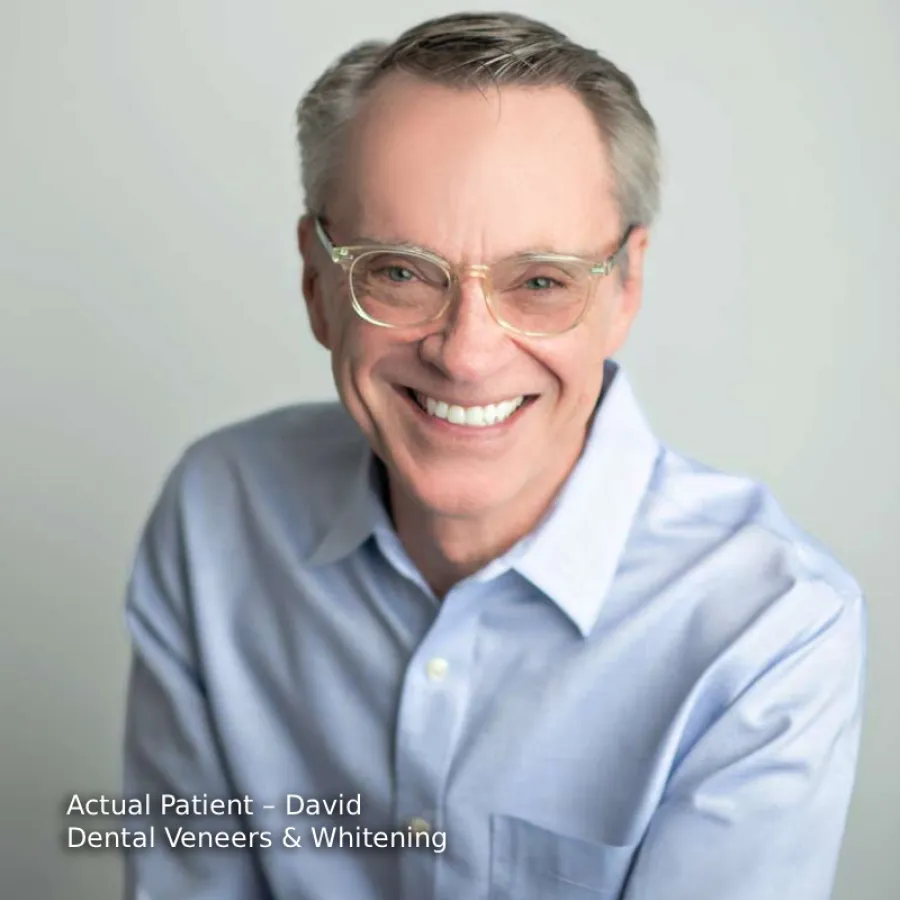 Smiling middle-aged man wearing glasses and a blue shirt showcasing bright white teeth after dental veneers and whitening.