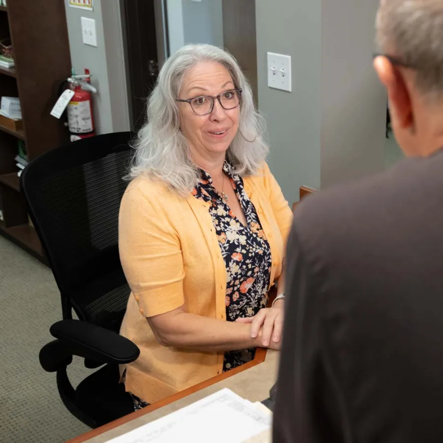 Mature woman in yellow cardigan talking to man at office desk, engaged in conversation during meeting