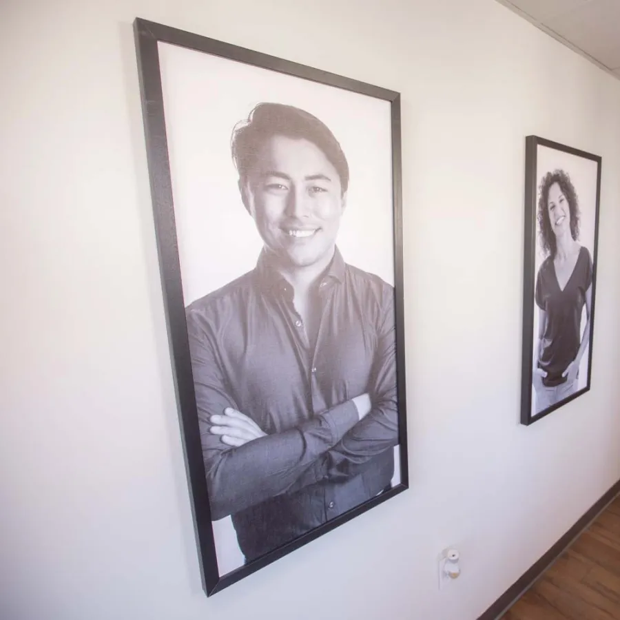 Hallway with wooden floor featuring black and white framed portraits of diverse smiling people on white walls.