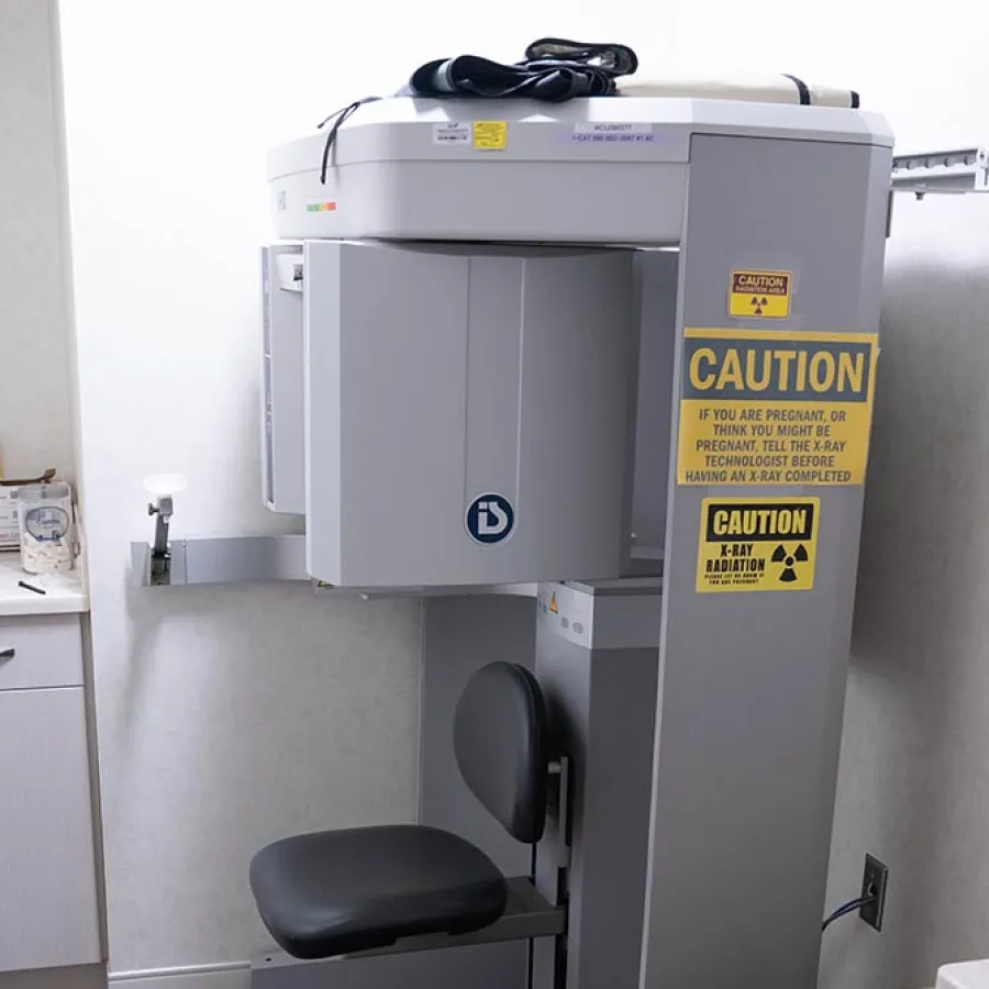 X-ray imaging machine with caution signs in a clean clinical room featuring a small countertop and storage cabinet.