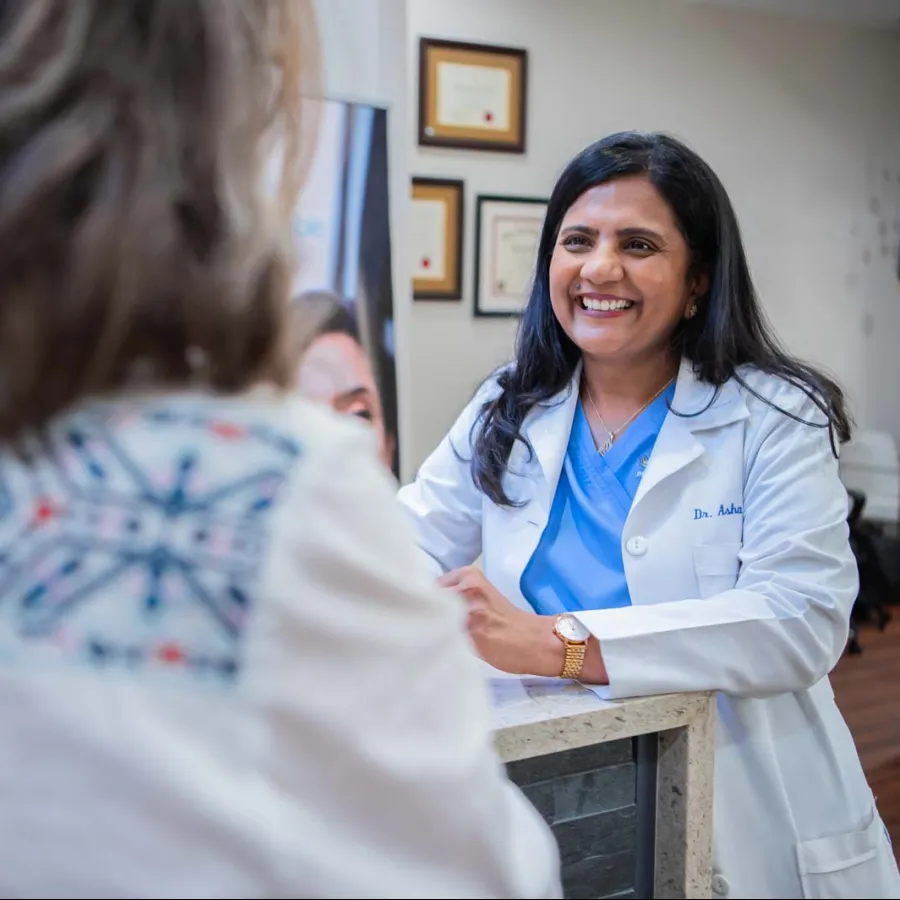 Smiling female doctor wearing a white coat consulting with a patient in a medical office.