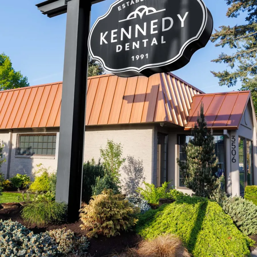 Kennedy Dental signpost with phone number outside a building with landscaped garden and copper roof