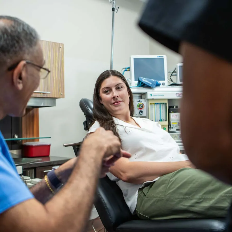 Doctor discussing treatment with a female patient seated in a medical office exam chair.