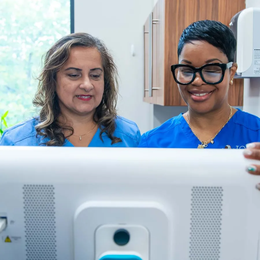 Two female healthcare professionals in blue scrubs looking at a computer screen in a medical office.