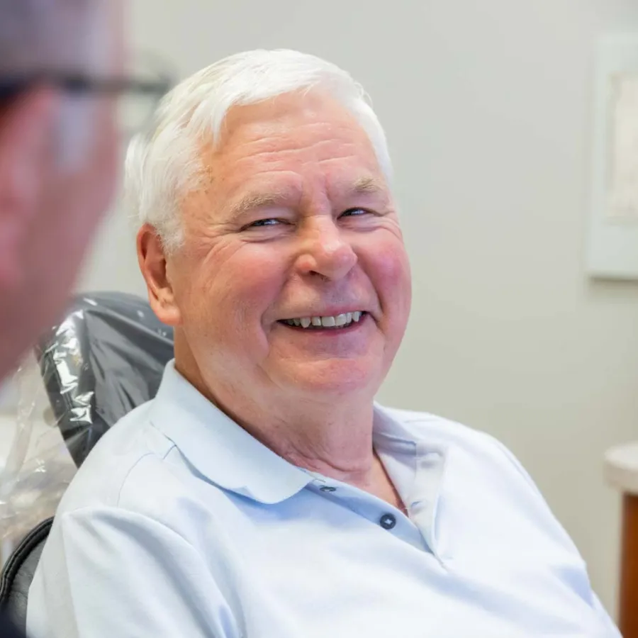 Elderly man smiling during a dental checkup with a dentist in a bright clinic setting.