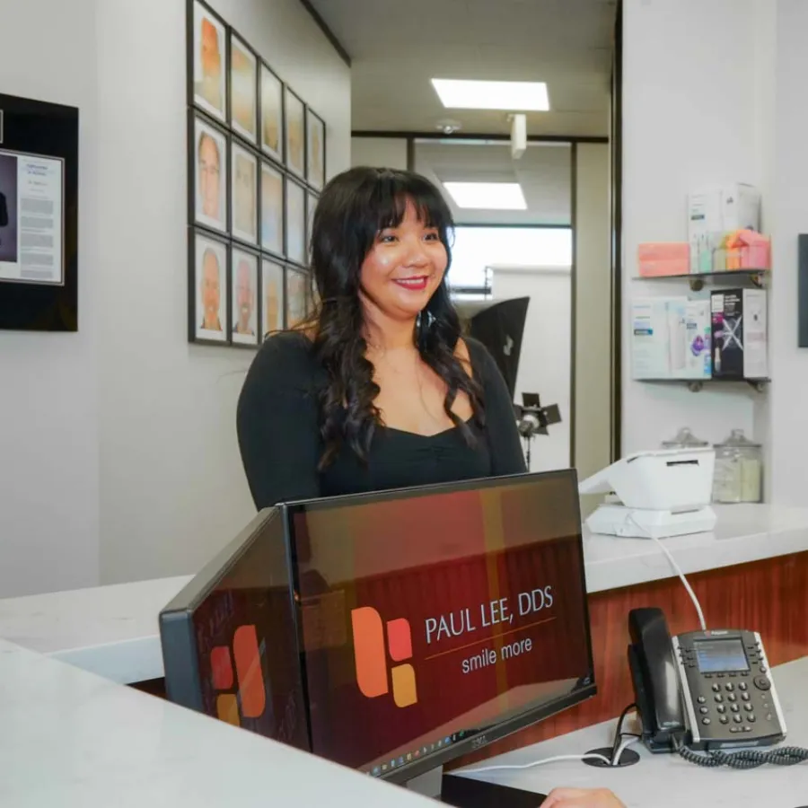 Receptionist smiling and assisting a patient at Paul Lee DDS dental office front desk.