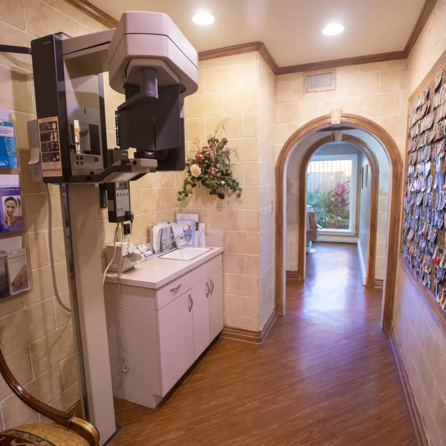 Dental X-ray machine and patient photo wall in a warm, inviting dental office hallway with wooden flooring.